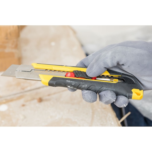 Photo of STANLEY FMHT10339-0 utility knife held in a gloved hand, yellow and black body with adjustable blade.