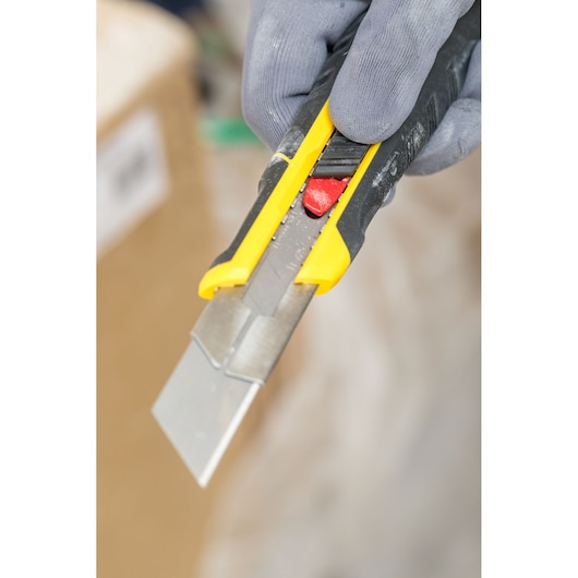 Photo of STANLEY FMHT10339-0 utility knife with yellow and black handle, close-up in gloved hand.