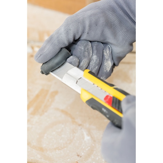 STANLEY FMHT10339-0 utility knife in use, yellow and black handle, close-up with gloved hands.