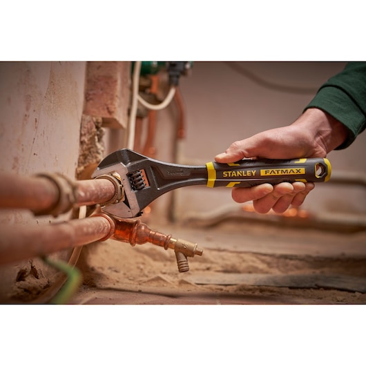STANLEY FMHT13125-0 adjustable wrench held on plumbing pipe, close-up in workshop setting.