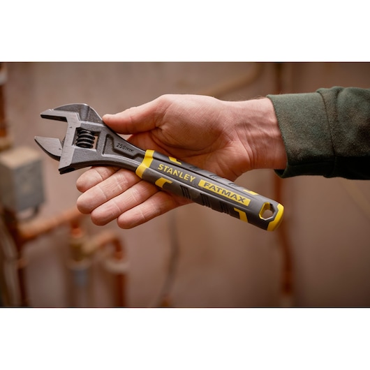 Photo of STANLEY FMHT13125-0 adjustable wrench with black and yellow handle, held in hand, plumbing background.