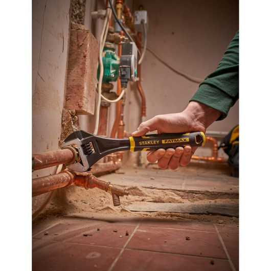 STANLEY FMHT13128-0 adjustable wrench with FATMAX handle used on copper pipes, close-up photo.