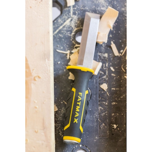STANLEY FMHT16693-0 chisel with black and yellow handle on workbench with wood shavings, top view.