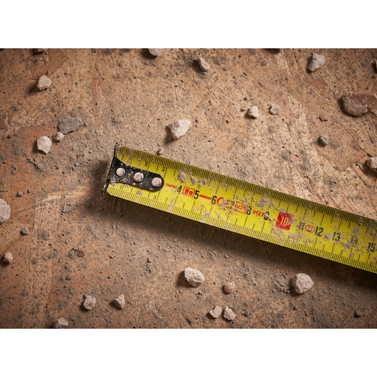 STANLEY FMHT33102 tape measure on dusty concrete with scattered small rocks, close-up view.