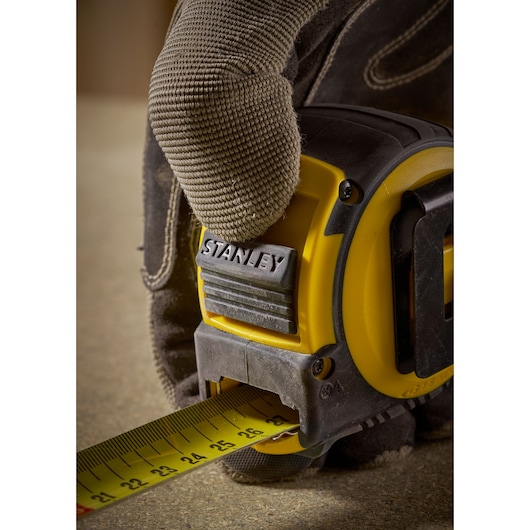 Photo of STANLEY FMHT33102 tape measure in use, yellow and black, shown being held by a gloved hand.