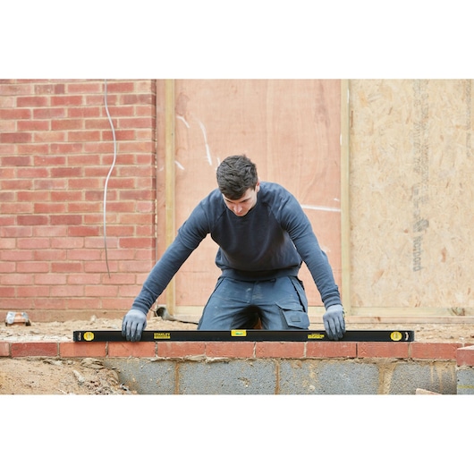 STANLEY FMHT42560-1 spirit level in use by builder, black body with yellow branding, outdoor construction setting.