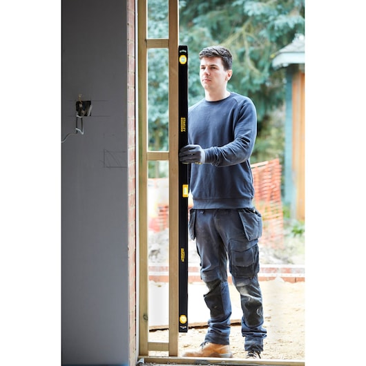 Person using STANLEY FMHT42560-1 spirit level at construction site, holding level vertically against wooden frame.