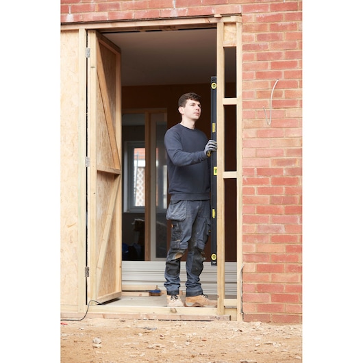 Photo of person using STANLEY FMHT42560-1 box beam level to check vertical line on wooden door frame at construction site.