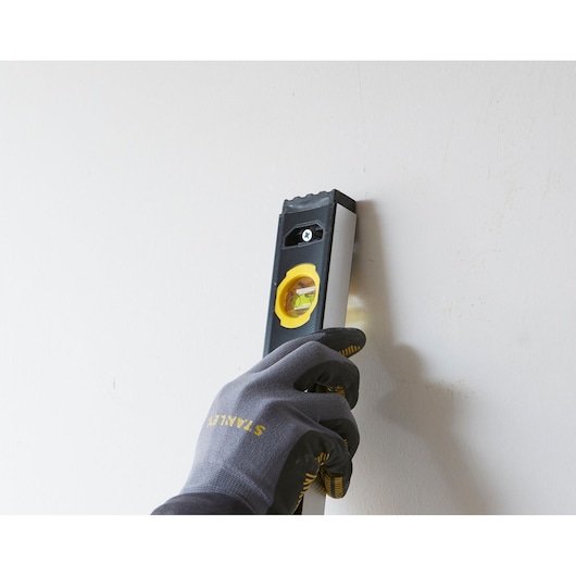 Photo of STANLEY FMHT42560-1 spirit level held vertically against a white wall by a gloved hand.