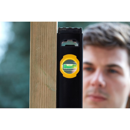 STANLEY FMHT42561-1 spirit level with yellow vial shown vertically against wooden post, outdoor setting.