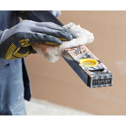 Photo of a gloved hand cleaning a STANLEY FMHT42561-1 level tool covered with debris, close-up view.