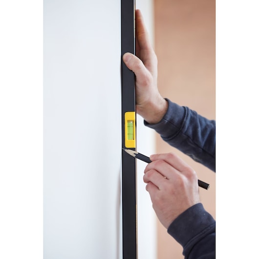 STANLEY FMHT42561-1 level tool held vertically against a wall, person marking with pencil.