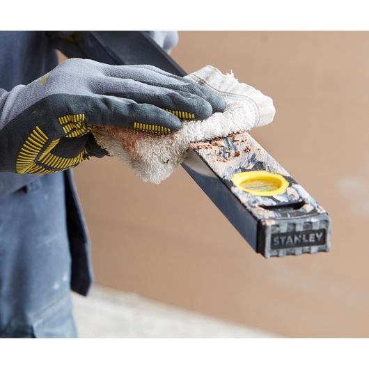 Photo of STANLEY FMHT42562-1 level being cleaned with a cloth by a gloved hand, construction context.