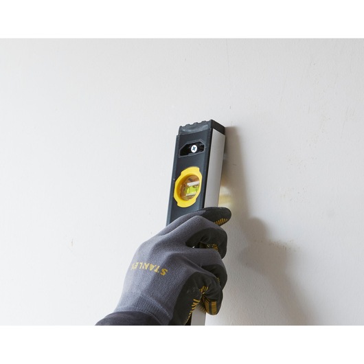 Photo of STANLEY FMHT42562-1 spirit level held vertically against a wall by a gloved hand.