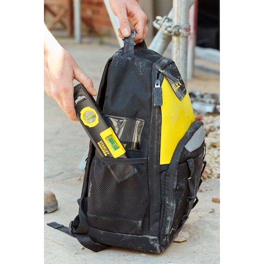 STANLEY FMHT42884-1 black and yellow tool backpack with side pocket, hand placing a spirit level inside.