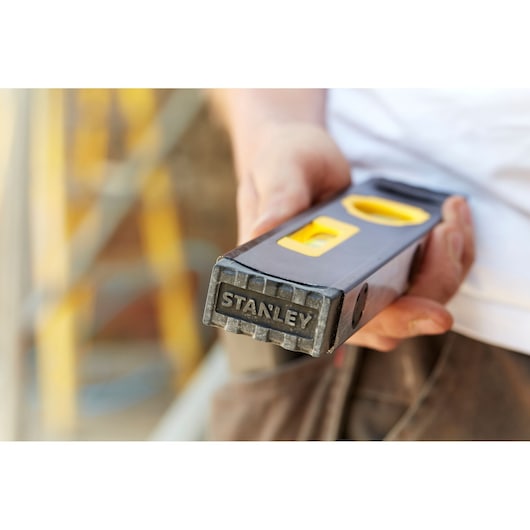 Photo of STANLEY FMHT42884-1 spirit level held in hand, black and yellow design, construction background.