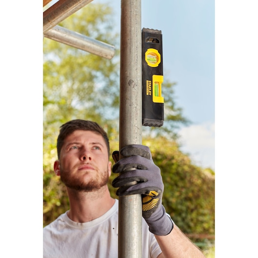 STANLEY FMHT42884-1 torpedo level used on a metal pole outdoors by a person wearing work gloves.