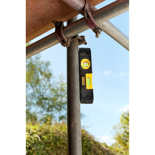 STANLEY FMHT42884-1 torpedo level with yellow vials, shown vertically attached to a metal pipe outdoors.