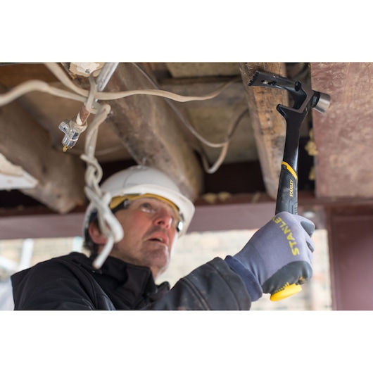 Stanley FMHT51367-2 claw hammer gripped by gloved hand during construction work, side angle.