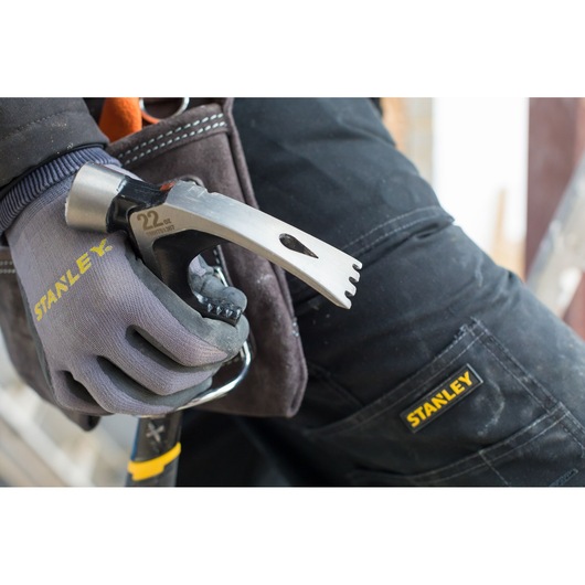 STANLEY FMHT51367-2 hammer held by a gloved hand beside work trousers with STANLEY logo, close-up view.