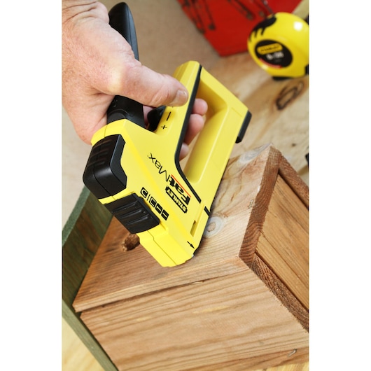 STANLEY FMHT6-70411 stapler in use on wood, yellow and black, close-up angle, hand holding tool.