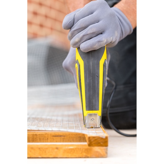 STANLEY FMHT6-75934 electric stapler close-up on wire mesh and wood, gloved hand operating tool.