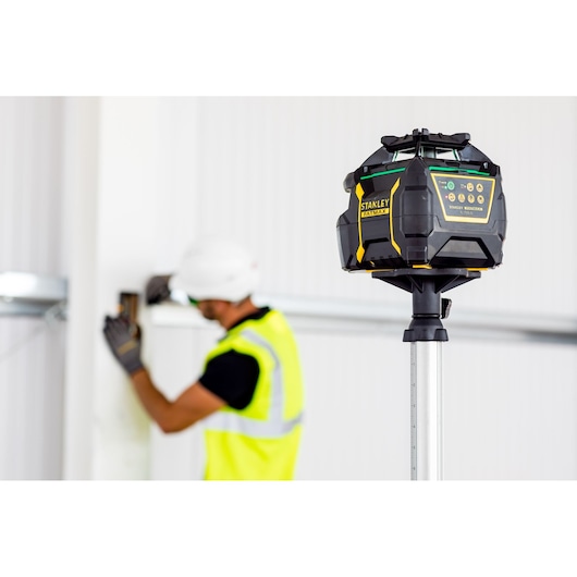 Photo of STANLEY FMHT77448-1 rotary laser level on tripod in a construction site, worker blurred in background.