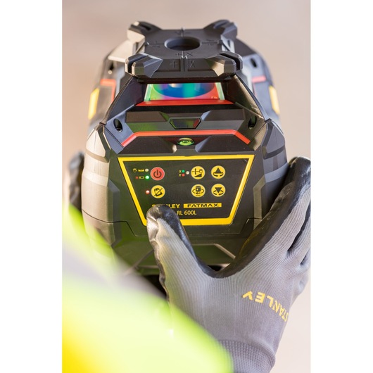 Photo of STANLEY FMHT77449-1 rotary laser level held by gloved hands, close-up of control panel.