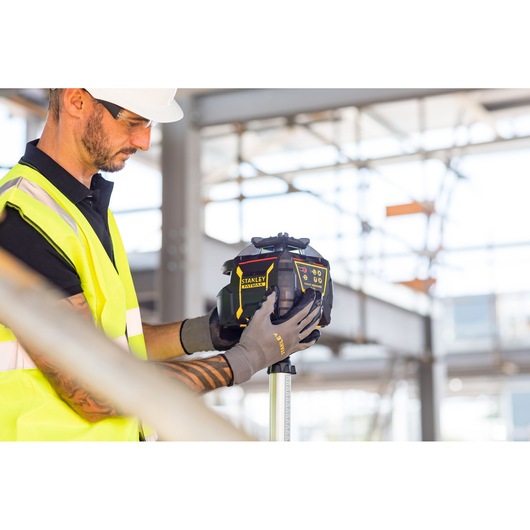 STANLEY FMHT77449-1 laser level held by worker in high-visibility vest at construction site.
