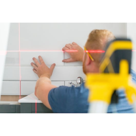 STANLEY FMHT77585-1 laser level in use for tiling wall, close-up showing red laser lines and worker's hands.