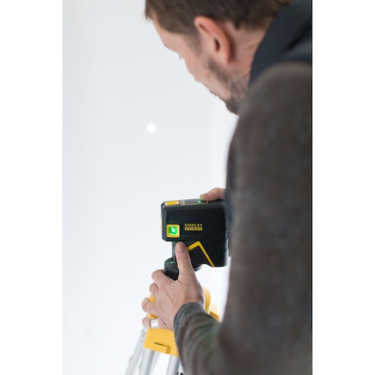 Photo of a person using STANLEY FMHT77596-1 laser level on a tripod, close-up of hand operating the device.