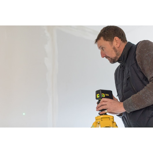 Photo of STANLEY FMHT77596-1 laser level on tripod, person adjusting device in indoor construction setting.