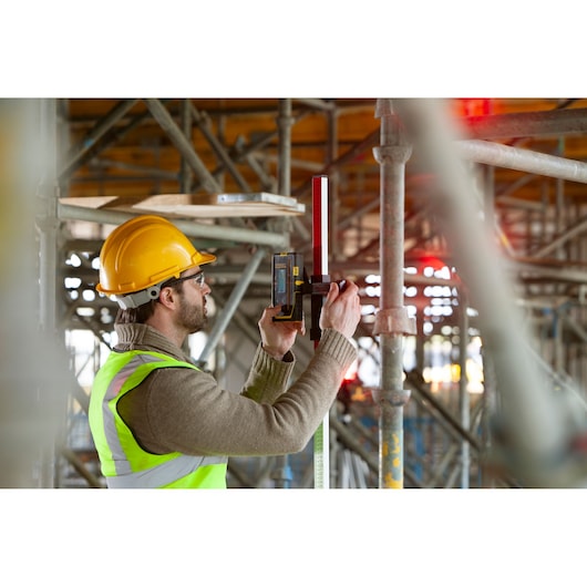 STANLEY FMHT77652-0 laser level used on construction site, held by worker in safety gear.