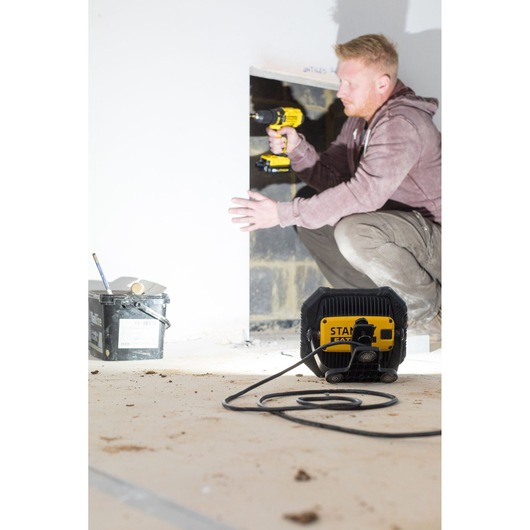 STANLEY FMHT81508-1 work light on floor in construction setting, cord extended, worker and tools in background.
