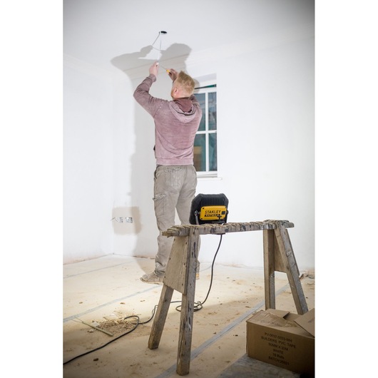 Photo of STANLEY FMHT81508-1 worksite power tool on wooden sawhorse, worker painting ceiling indoors.