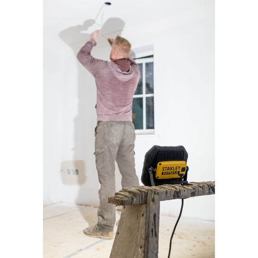 STANLEY FMHT81508-1 work light on wooden sawhorse, illuminating man working on white ceiling in unfinished room.