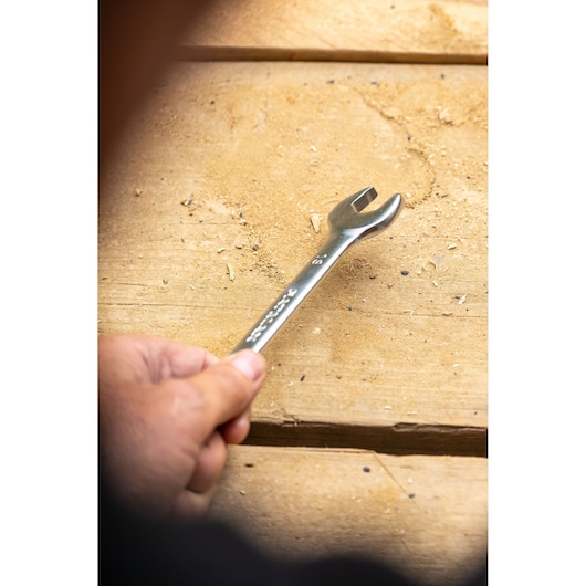 Photo of STANLEY FMMT13039-0 wrench held in hand on wooden surface, open-end design visible.