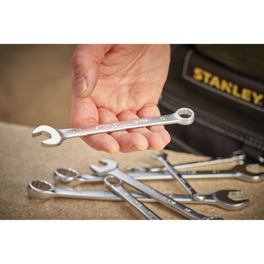 STANLEY FMMT13042-0 combination wrench held in hand, several wrenches on table, close-up photography.