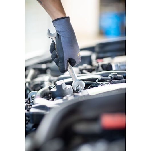 Photo of STANLEY FMMT13070-0 wrench used on car engine, mechanic wearing gloves, close-up.