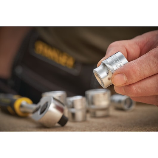 STANLEY FMMT17210-0 socket set photography, close-up of hand holding socket with ratchet and other sockets nearby.