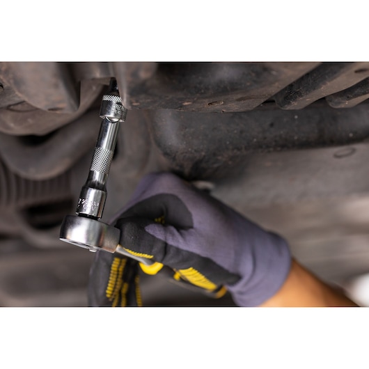 STANLEY FMMT25131-0 ratchet wrench in use under vehicle, close-up photography, tool held by gloved hand.