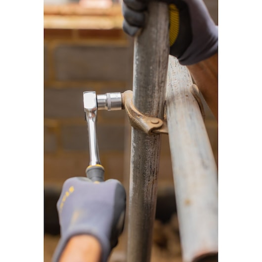 Photo of STANLEY FMMT82678-0 ratchet being used to tighten a metal pipe clamp in a construction setting.