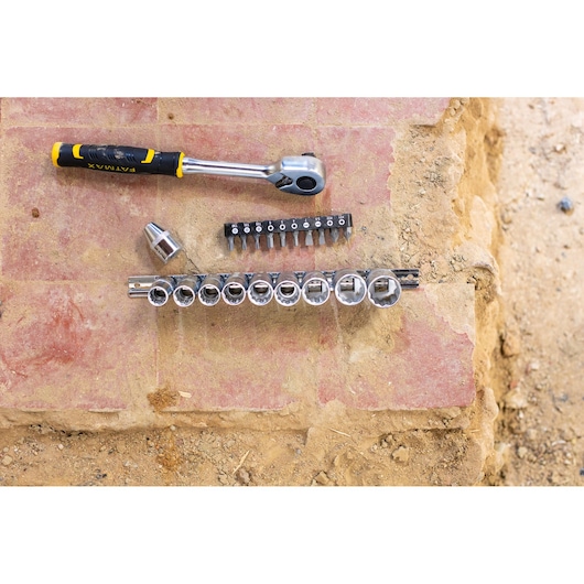 STANLEY FMMT82679-0 ratchet wrench and socket set with bits, top view on outdoor stone surface.