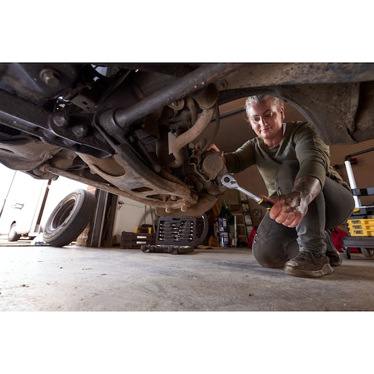 STANLEY FMMT82827-1 socket and wrench set in use under a car in a garage, mechanic working on suspension.