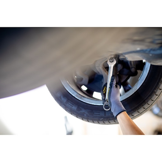 STANLEY FMMT82849-0 ratcheting wrench tightening bolt on car suspension, gloved hand visible, close-up.