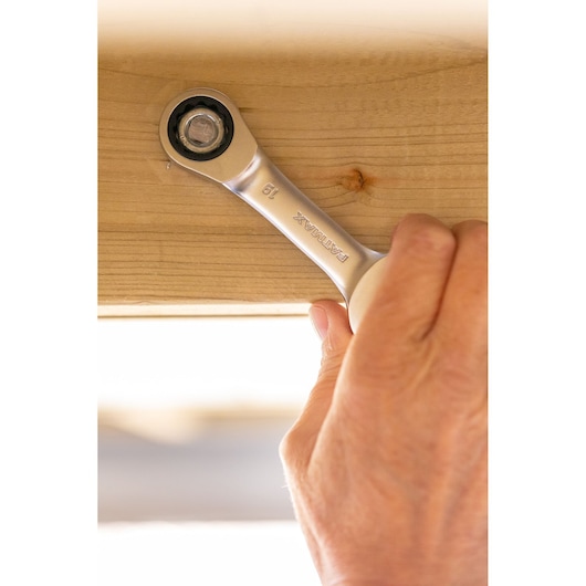 STANLEY FMMT82900-0 ratcheting wrench used to tighten a bolt on wood, close-up of hand and tool.
