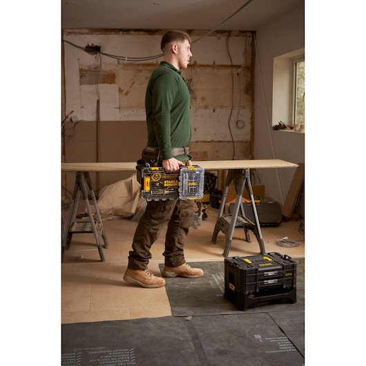 Photo of STANLEY FMMT98101-0 tool organiser in clear and black plastic, shown being carried on a construction site.