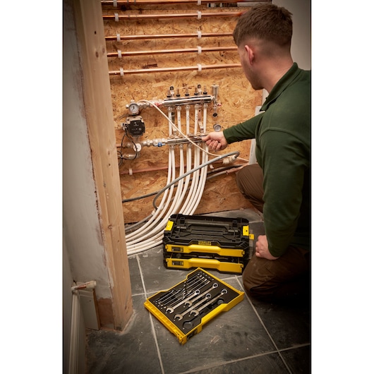 STANLEY FMMT98107-1 tool set and toolbox used by a person fixing pipes near a wall, plumbing context.