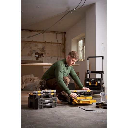Person assembling STANLEY toolboxes in a workspace with unfinished walls and various storage containers around.