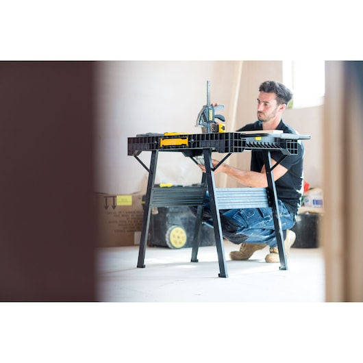 Photo of STANLEY FMST1-75672 workbench in use at construction site, person kneeling beside black folding table.